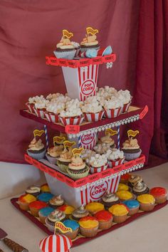 a three tiered tray with cupcakes and popcorn on it next to a red curtain