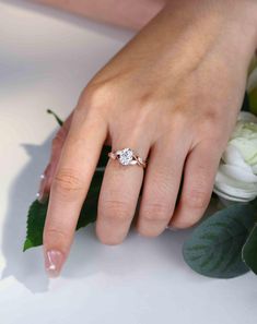 a woman's hand with a ring on her finger and flowers in the background