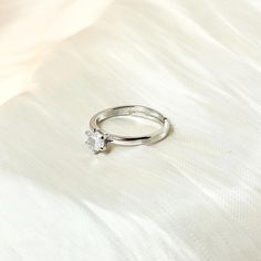 a diamond ring sitting on top of a white bed sheet in front of a pillow