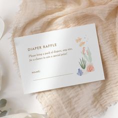 a diaper raffle card sitting on top of a blanket next to some flowers