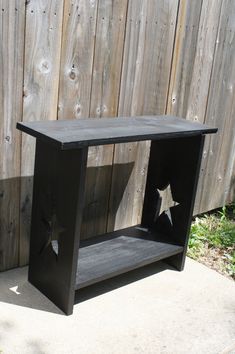 a black wooden shelf sitting on top of a cement floor next to a fence and grass