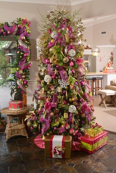 a decorated christmas tree with pink and green decorations on it's top, surrounded by presents