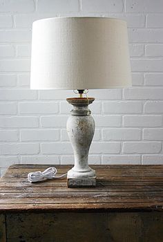 a white lamp sitting on top of a wooden table next to a brick wall with a cord plugged into it