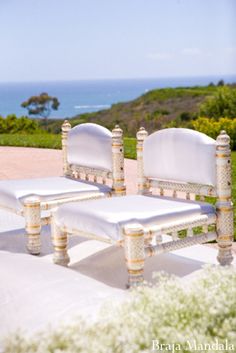 two white chairs sitting next to each other on top of a lush green field near the ocean