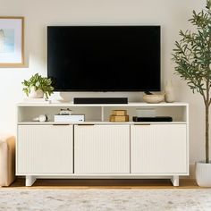 a flat screen tv sitting on top of a white cabinet next to a potted plant