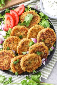 several crab cakes on a plate with tomatoes, onions and lettuce