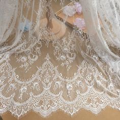 white lace with pink flowers on it sitting on top of a wooden table next to a vase