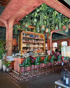 a bar with lots of green chairs and plants hanging from it's ceiling over the bar