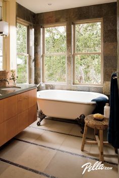 a bathroom with a claw foot tub, sink and large windows in the wall above it