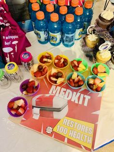 a table topped with lots of cupcakes and fruit next to bottles of water