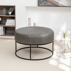 a living room with a round ottoman and bookshelf in the background, on carpeted flooring