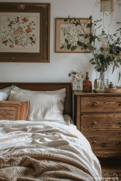 a bed with white linens and flowers on the headboard next to two framed pictures