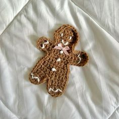 a crocheted teddy bear laying on top of a white bed sheet with pink bow