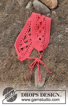 a pink crocheted hat laying on the ground next to some rocks and stones