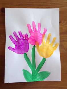 three handprints on paper with flowers in the middle and one painted pink, yellow and green