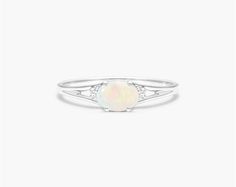 14K White Gold Oval Opal and Diamond Accent Birthstone Ring. The birthstone of October, opal was known in ancient times as the Queen of Gems because it encompasses colors of all other gems. Opal is a symbol of hope and loyalty and is said to bring love, passion, spontaneity and strength to those who wear it. This east-west opal ring with accent diamonds is the perfect piece for your special someone White Opal Birthstone Ring With Gemstone, Classic White Opal Birthstone Ring, Classic White Opal Ring With Birthstone, Fine Jewelry White Opal Birthstone Ring, Heirloom White Opal Ring Oval Cabochon, Heirloom White Opal Ring, Opal Birthstone Ring In White Gold, White Opal Ring With Round Stone, Heirloom Oval Opal Ring With Accent Stones