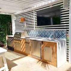 an outdoor kitchen with grills, sink and television mounted to the side of it