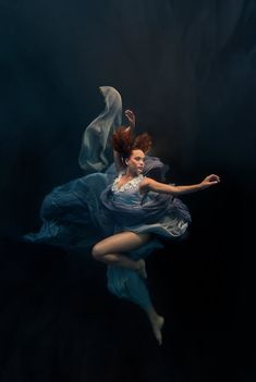 a woman is floating in the water wearing a blue dress and holding her arms out