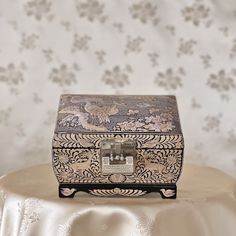 an ornate wooden box sitting on top of a white table cloth covered table with floral wallpaper