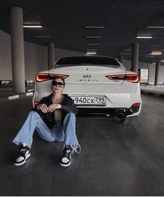 a man sitting on the back of a white car in an empty parking garage with his legs crossed