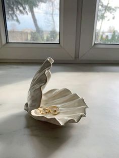 two wedding rings are placed in a shell on the floor next to a pair of windows