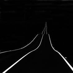 a black and white photo of an empty road in the dark with no cars on it