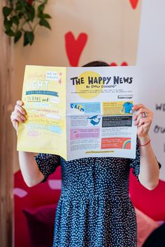 a woman holding up a newspaper with the words happy news written on it in front of her face