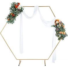 a white backdrop with flowers and greenery on it, along with a gold hexagonal frame