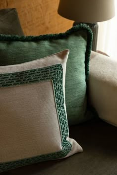 two green and white pillows sitting on top of a couch next to a light fixture