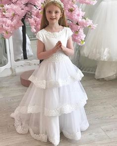 Buy jewel neck white first communion dress with layered skirts online at JJsprom.com Tiered Princess Dress For Wedding, White Princess Style Tiered Dress, White Tiered Wedding Dress, Wedding Dress With Layered Tiered Skirt, Wedding Dress With Tiered Skirt And Layered Hem, Wedding Dress With Layered Hem And Tiered Skirt, White Tulle Dress With Tiered Skirt, Elegant White Layered Dress, White Layered Dress With Tiered Skirt