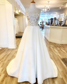 a white wedding dress on display in a store with wooden floors and chandelier