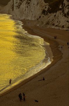 people are walking on the beach near the water's edge and cliffs in the background