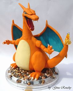 an orange and blue dragon figurine sitting on top of some rocks with its mouth open