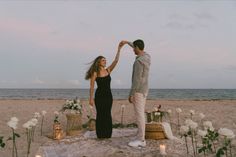 a man and woman dancing on the beach with candles in front of them, surrounded by flowers