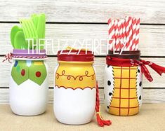 three painted mason jars with spoons and forks in them, sitting on a table