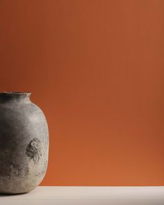 a gray vase sitting on top of a white table next to an orange wall with a black cat sticking out of it