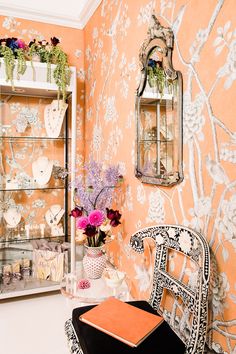 a chair sitting in front of a wall with flowers on it and a mirror behind it