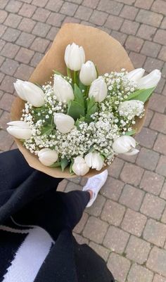 a bouquet of white tulips and baby's breath is held by someone