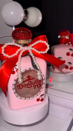 a pink bottle with a red bow and some pearls on it's top is sitting on a shelf