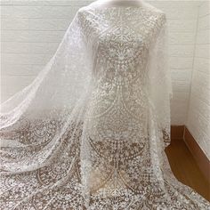 a white lace dress on display in front of a brick wall and wooden flooring