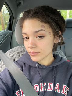 a young woman sitting in the back seat of a car wearing a hoodie with writing on her forehead