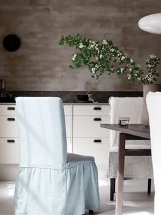 a dining room table and chair covered in a blue cover next to a vase with white flowers