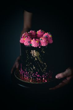 a person holding a cake with pink frosting and sprinkles