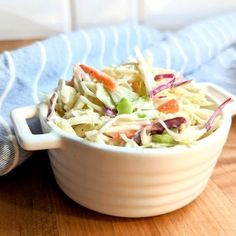 a white bowl filled with coleslaw sitting on top of a wooden table next to a blue towel