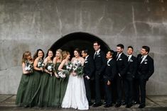 a group of people standing next to each other in front of a stone wall holding bouquets