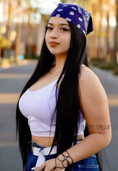 a woman with long black hair wearing a bandana and blue jeans is standing in the street