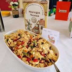 there is a bowl of pasta on the table with a book in the back ground