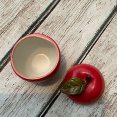 a red tomato and a white bowl on a wooden table