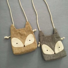 two small bags with foxes on them are hanging from strings, one is brown and the other is gray