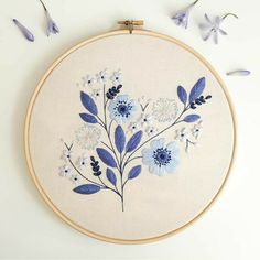 a blue and white floral embroidery pattern on a beige hoop with purple flowers in the background